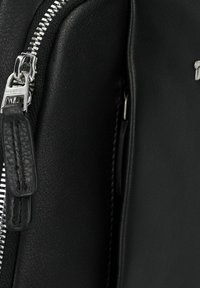 Bolso de cuero negro con una cremallera plateada y un tirador de cuero. La textura es suave con detalles de costura mínimos.