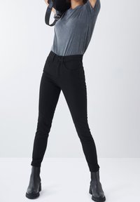 Jeans ajustados negros con un diseño de cinco bolsillos, combinados con una camiseta gris de manga corta y botines negros. Textura de tela suave.