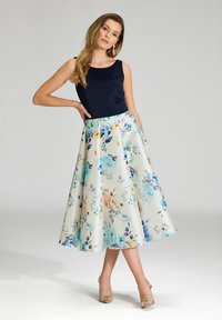 Jupe midi florale dans des couleurs pastel avec un fond crème, associée à un haut sans manches bleu marine, présentant une taille cintrée et une silhouette évasée.