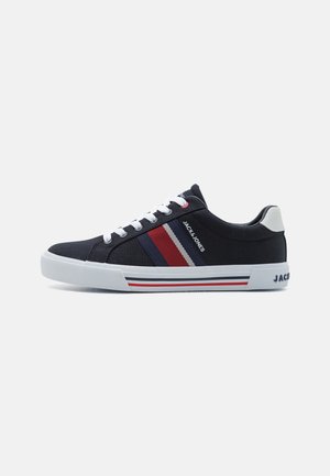 Des baskets en toile bleu marine présentent des lacets blancs, des accents rayés rouge et blanc, et une semelle en caoutchouc blanc avec un logo au talon.
