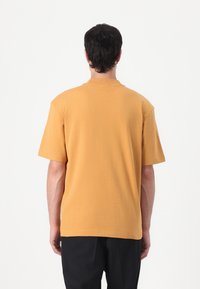 Kortærmet t-shirt i sennepsgul bomuld, ribbet rund hals, afslappet pasform, glat tekstur og ingen synlige mønstre eller grafik.