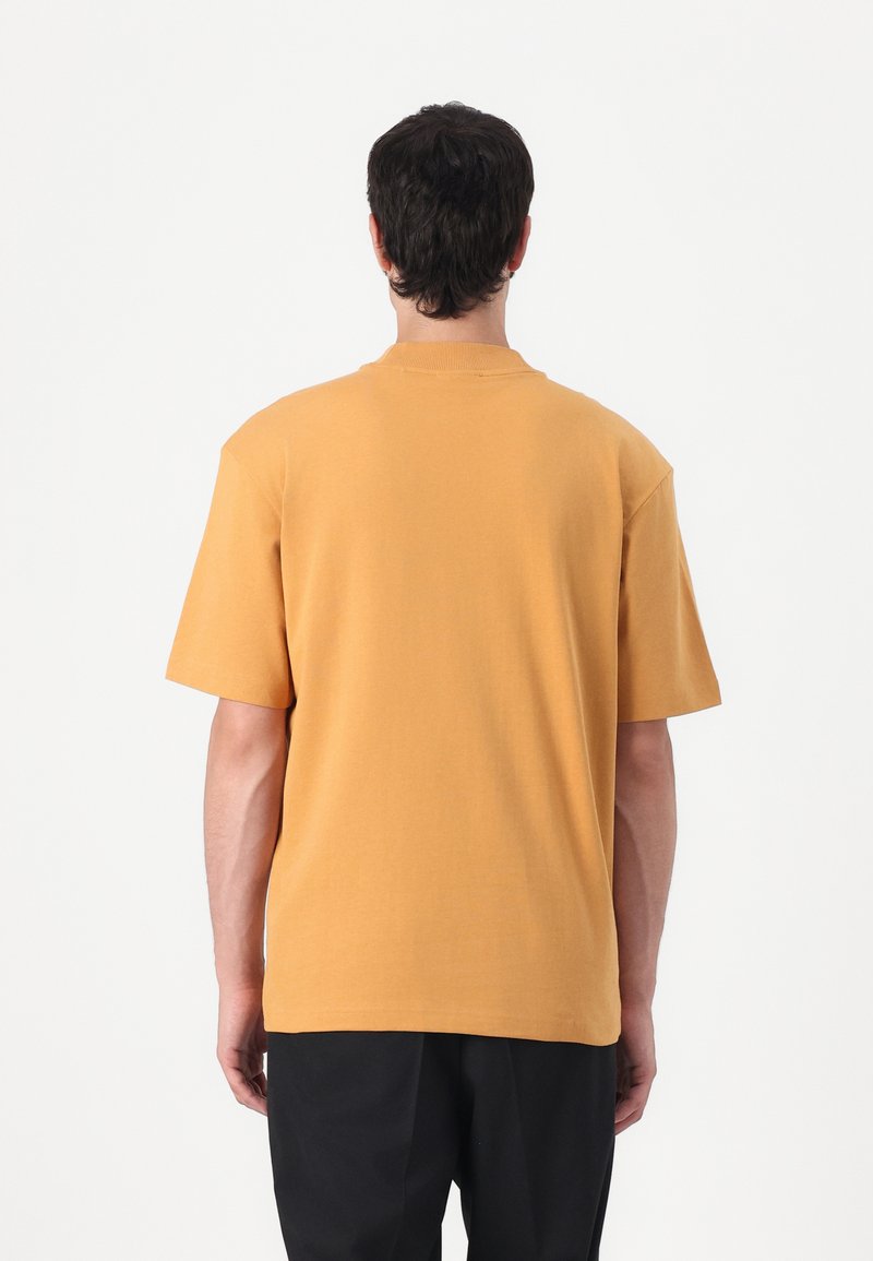 T-shirt med kort ärm i senapsgul bomull, ribbad rundhals, avslappnad passform, slät struktur och utan synliga mönster eller grafik.