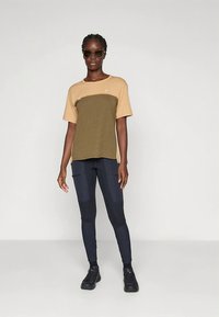 Šviesiai ruda ir alyvuogių žalios spalvos trumpomis rankovėmis marškinėliai su tamsiomis tamprėmis su kišenėlėmis, baigti juodais sportbačiais ir akiniais nuo saulės.