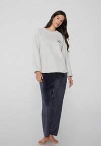 Sudadera de felpa gris con cuello redondo y texto negro, combinada con pantalones de pana azul marino con canalé. Textura suave, corte casual.