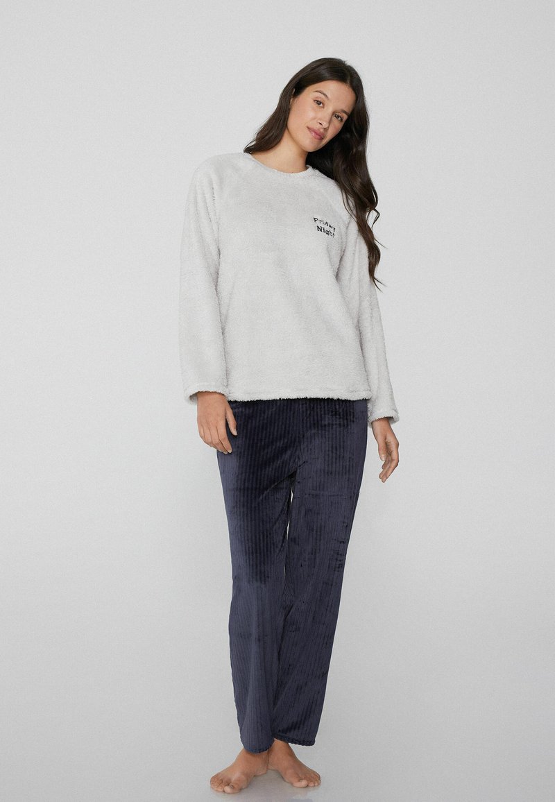 Sudadera de felpa gris con cuello redondo y texto negro, combinada con pantalones de pana azul marino con canalé. Textura suave, corte casual.
