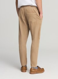 Pantaloni di velluto a coste marrone chiaro con vestibilità slim, vita elasticizzata, tasche laterali e una tasca applicata sul retro; abbinati a calzature marroni.