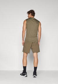 Ελαιόχρωμο αμάνικο πουκάμισο σε συνδυασμό με ταιριαστά σορτς. Το ύφασμα φαίνεται μαλακό με χαλαρή εφαρμογή. Μαύρα αθλητικά παπούτσια ολοκληρώνουν την εμφάνιση.