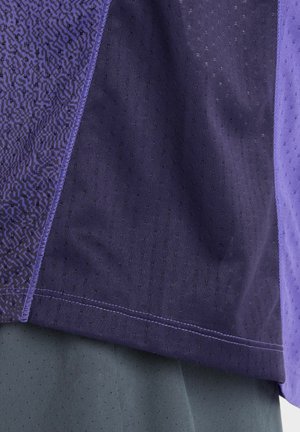 Close-up of purple and lavender fabric panels with textured patterns and dotted knit details on garment edges.