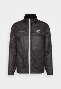 Musta Nike-takki, jossa on tekstuuripinta, valkoinen vetoketju ja yksityiskohdat, korkea kaulus ja pitkät hihnat. Takissa on logot rinnassa.