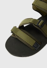 Olivengrønne sandaler med to justerbare stropper, lavet af nylonstof, og med en tekstureret sort gummisål og kontrastende sorte metaldele.