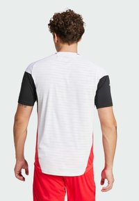 Camisa atlética para hombre con mangas cortas negras y cuerpo blanco con acentos rojos. Fabricada con un tejido suave y ligero, presenta un patrón sutil.