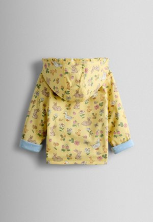 Sárga esőkabát kapucnival, amely nyuszis, madaras és virágos mintával díszített. Kék pöttyös mandzsettái kontrasztos hangsúlyt adnak.