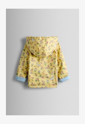 Dzeltens lietusmētelis ar kapuci, uz kura ir zaķu, putnu un ziedu raksts. Zili punktiņi uz aprocēm rada kontrastējošu akcentu.