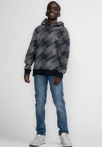 Felpa navy con pattern geometrico bianco, polsini e orlo a coste, vestibilità comoda, abbinata a jeans azzurri e sneakers grigie.