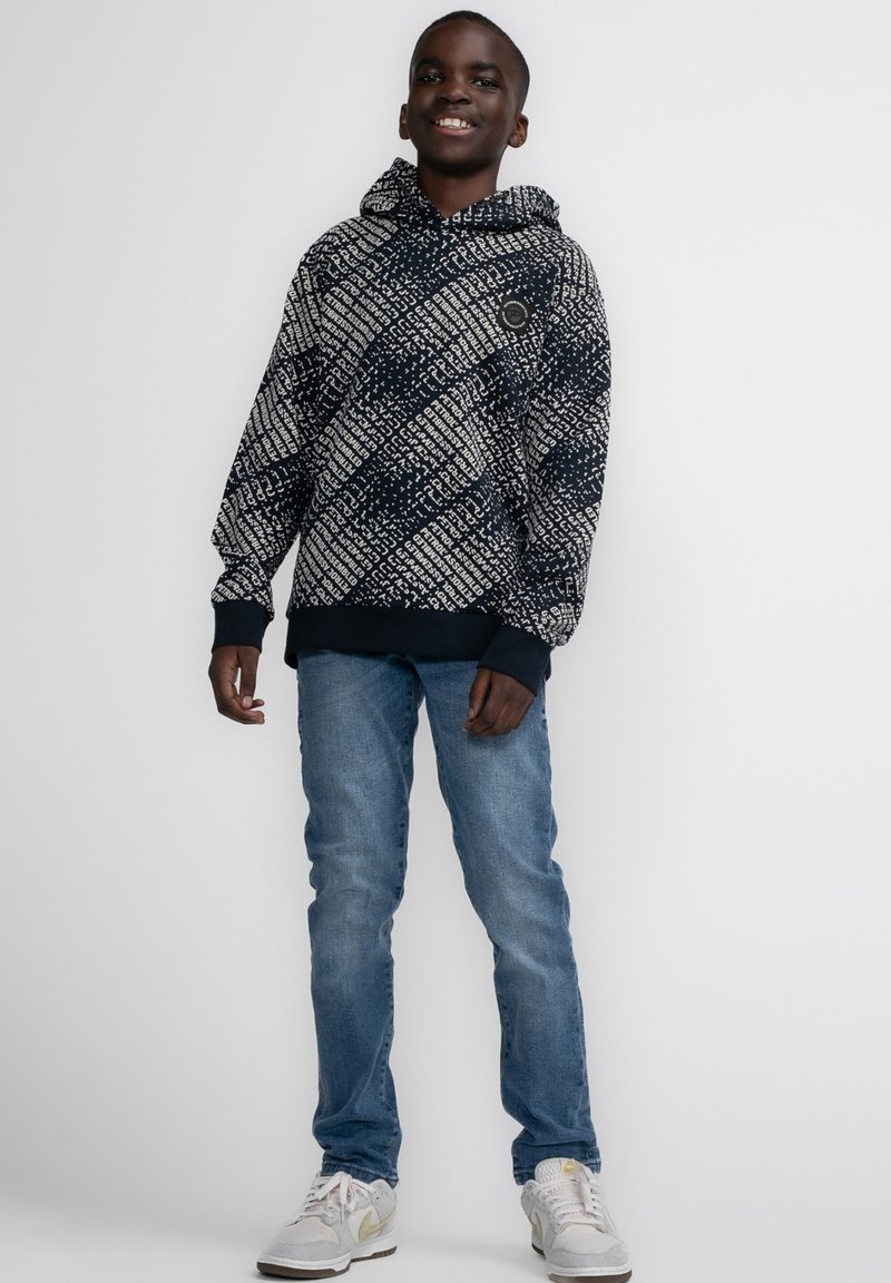 Felpa navy con pattern geometrico bianco, polsini e orlo a coste, vestibilità comoda, abbinata a jeans azzurri e sneakers grigie.