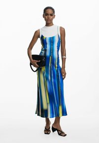 Rochie fără mâneci, cu dungi albastre și galbene, având un top ajustat și o fustă fluidă, asortată cu o poșetă neagră și sandale cu toc spiral.