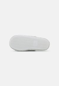 Shoe sole with a white rubber base, featuring a textured zigzag pattern. Light gray fabric upper with a rounded toe and minimal design details.