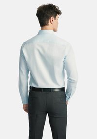 Jasnoniebieska koszula z długim rękawem o dopasowanym kroju, z tylnym karczkiem i mankietami na guziki, noszona z ciemnoszarymi spodniami garniturowymi i czarnym paskiem.