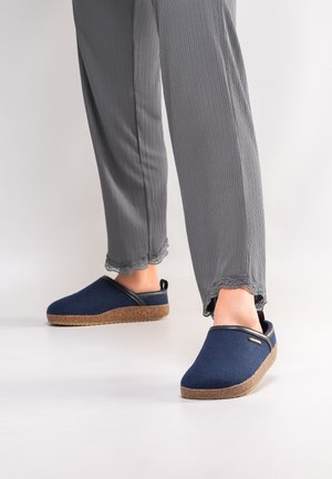 Feet wearing navy blue slip-on shoes with textured brown soles, paired with gray ribbed pants with lace-trimmed cuffs.