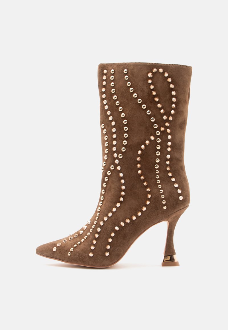 Botín de ante marrón hasta el tobillo con punta afilada, adornado con patrones en espiral de tachuelas metálicas y un tacón alto delgado con un acento dorado.