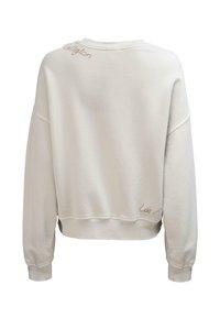 Jasnobeżowa bluza z długimi rękawami, ściągaczami na mankietach i dole oraz małym haftowanym napisem w pobliżu dekoltu i dolnej krawędzi.