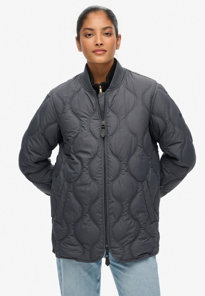 Giubbotto bomber trapuntato grigio scuro con zip frontale, collo a costine e tasche laterali. Presenta una texture liscia e sottili motivi ondulati.