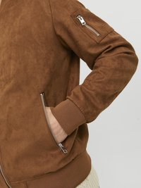 Chaqueta bomber de ante marrón con puños y bajo acanalados. Cuenta con un bolsillo con cremallera en ángulo en la manga izquierda y bolsillos laterales.