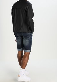 Svart lättviktsjacka med en enkel design, kombinerad med mörka denimshorts med upprullade fållar och vita sneakers.