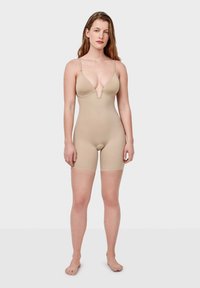 Bodysuit beige con escote en V profundo, tirantes ajustables y longitud hasta el muslo. Confeccionado en tela suave, presenta un diseño ajustado.