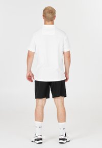 Vit kortärmad polo, mjukt tyg, rund krage, tillsammans med svarta shorts. Lätta skor och vita strumpor kompletterar outfiten.