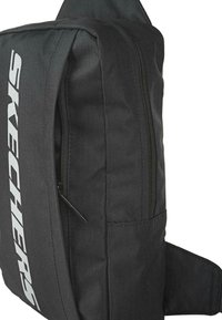 Bolso de hombro de tela negra con forma rectangular, que cuenta con un compartimento con cremallera y un gran logo blanco de "SKECHERS" en el lateral.