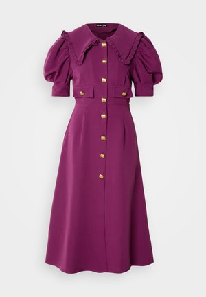 Robe violette avec un grand col, des manches bouffantes et des accents de boutons dorés. Elle dispose de deux poches avant et d'une jupe mi-longue. Texture lisse.