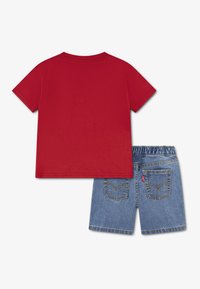 Κόκκινο βαμβακερό μπλουζάκι με κοντά μανίκια δίπλα σε μπλε τζιν σορτς με ζώνη στη μέση και δύο πίσω τσέπες με ραφές λεπτομέρειες.