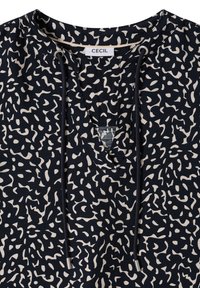 Chemise noire et blanche à motifs abstraits avec col en V, cordons avec embouts métalliques, et une étiquette de marque "CECIL" à l'intérieur du col.