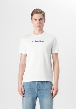 Balts kokvilnas t-krekls ar īsām piedurknēm un apaļu apkakli. Aprīkots ar "Calvin Klein" logotipu purpura krāsā krūtīs.