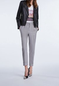 Veste en cuir noir de motard sur un T-shirt graphique blanc, associée à un pantalon à carreaux gris et des escarpins pointus noir et argent.