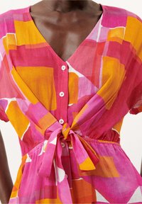 Abito corto in tessuto leggero con un motivo geometrico rosa, arancione e bianco, scollatura a V, chiusura con bottoni frontali e dettaglio in vita annodato.