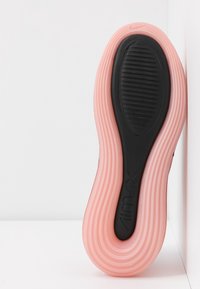 Podeszwa różowego sneakersa Nike Air Max z czarną teksturowaną podeszwą antypoślizgową, skierowaną ku przodowi na białym tle.