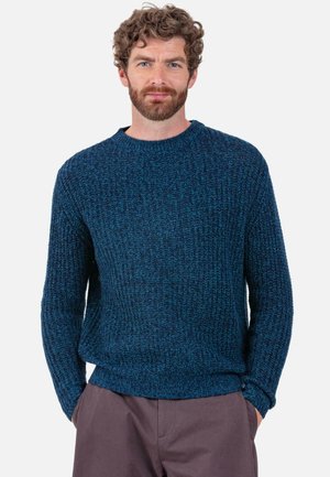 Pull en tricot bleu avec un motif texturé, col rond et manches longues, associé à un pantalon beige ample.