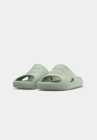 Une paire de sandales ouvertes à bout ouvert, de couleur vert clair, à enfiler, avec des trous de ventilation et le logo "Tommy Jeans" sur le devant.