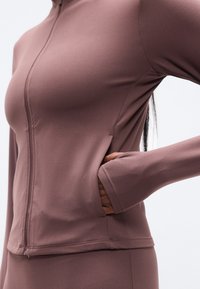 Μώβ τζάκετ με φερμουάρ, με εφαρμοστή σχεδίαση, μακριά μανίκια, πλαϊνές τσέπες και ομαλό, ελαστικό ύφασμα για άνεση.