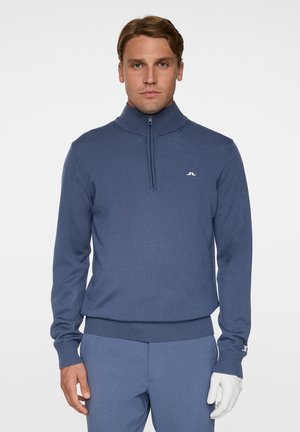 Heren blauwe gebreide pullover met een hoge kraag en een kwart ritssluiting. Beschikt over geribbelde manchetten en onderrand, en een klein wit logo op de linkerborst.