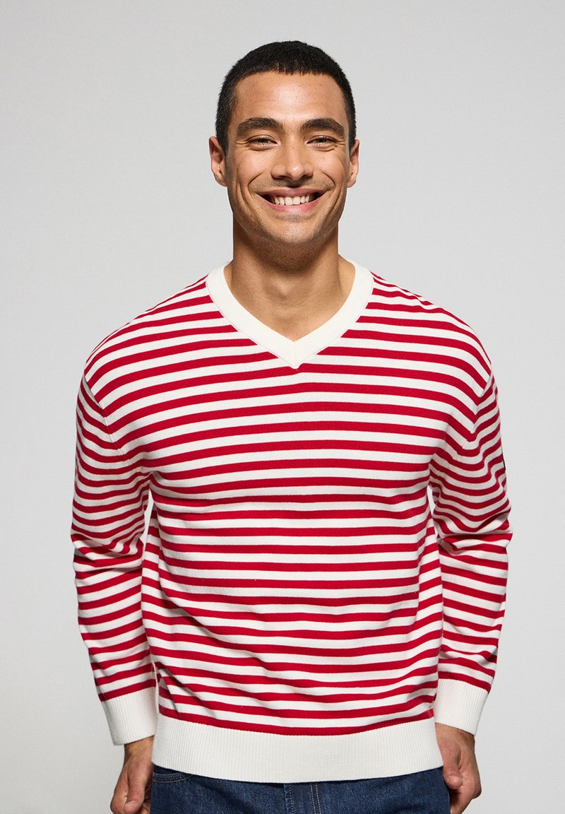 Rood-wit gestreept trui met een V-halsontwerp, gebreide textuur en geribbelde manchetten. Draagt met blauwe spijkerbroeken.