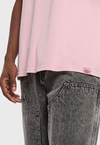 Ljusrosa bomullströja med rak fåll och liten logotagg, matchad med mörkgrå denimbyxor med stora framfickor.