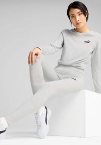 Helle graue Langarmbluse und Leggings mit schmalem Schnitt, akzentuiert durch ein schwarzes Logo. Weiße Sneakers runden den Athleisure-Look ab.