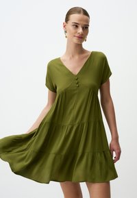 Grünes, gestuftes Kleid mit kurzärmeligen, V-Ausschnitt und Knopfdetails an der Vorderseite. Leichter Stoff mit subtiler Textur.