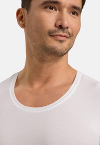 White crew-neck t-shirt made of smooth fabric, featuring a close fit and a clean neckline. Skin tone visible under the shirt.