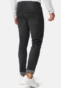 Jeans de mezclilla gris oscuro con un corte ajustado, diseño de cinco bolsillos, puños enrollados y una textura suave. Llevados con zapatillas blancas.