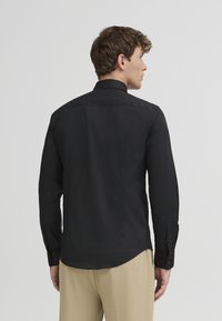 Schwarzes Langarmhemd mit Kragenentwurf, glatter Textur und Knopfmanschetten. Es hat einen abgerundeten Saum und ein minimalistisches Design.