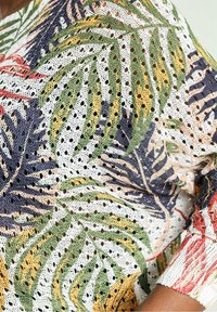 Jersey de punto con tejido abierto y un patrón de hojas de palma multicolor en verde, rojo, amarillo y azul marino sobre un fondo blanco.